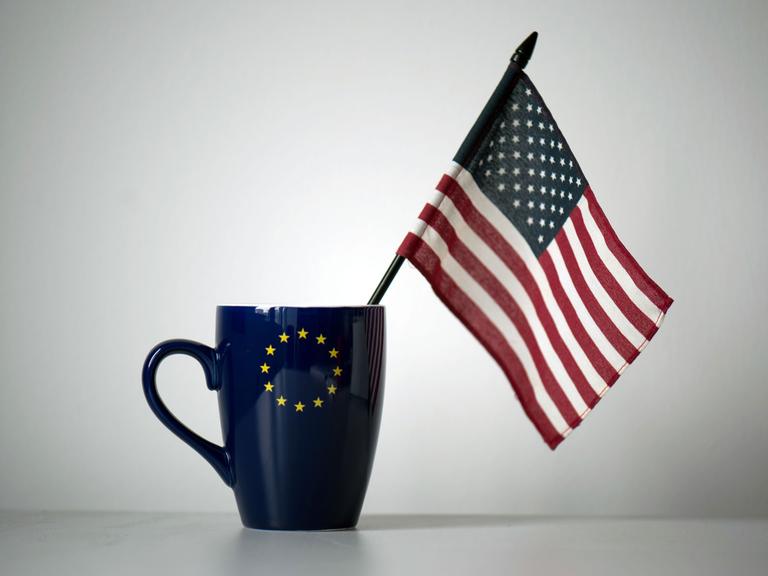 In einer Tasse mit einem EU-Symbol steckt eine US-Fahne, aufgenommen in einem Büro in Dresden.