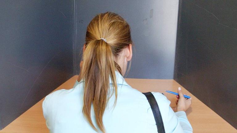 Eine Frau sitzt in der Wahl-Kabine mit dem Wahl-Zettel Eine Frau sitzt in der Wahl-Kabine mit dem Wahl-Zettel