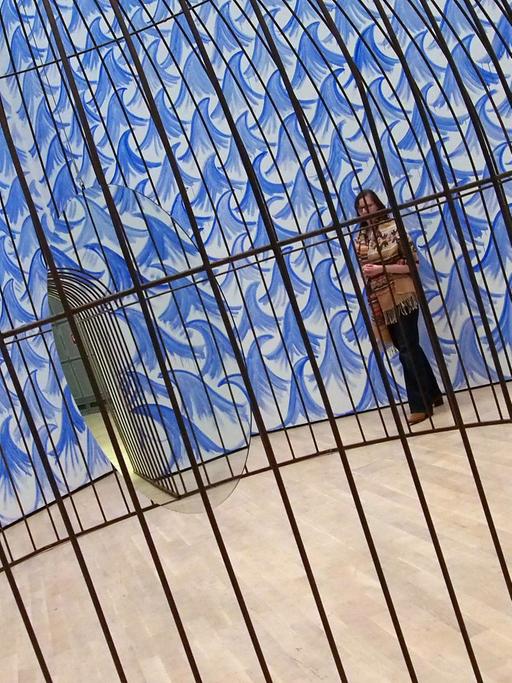 Eine Besucherin und ein Museumsmitarbeiter stehen am 11.11.2015 in der Kunstausstellung "Jeppe Hein. This Way" im Kunstmuseum Wolfsburg vor einem riesigen Käfig, in dem ein Spiegel kreist.