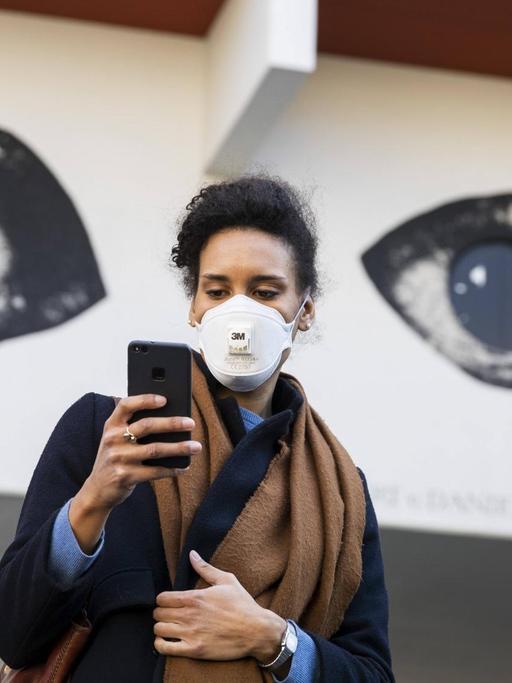 Eine Junge Frau schaut auf ihr Handy mit den Augen eines Grafitti im Hintergrund.