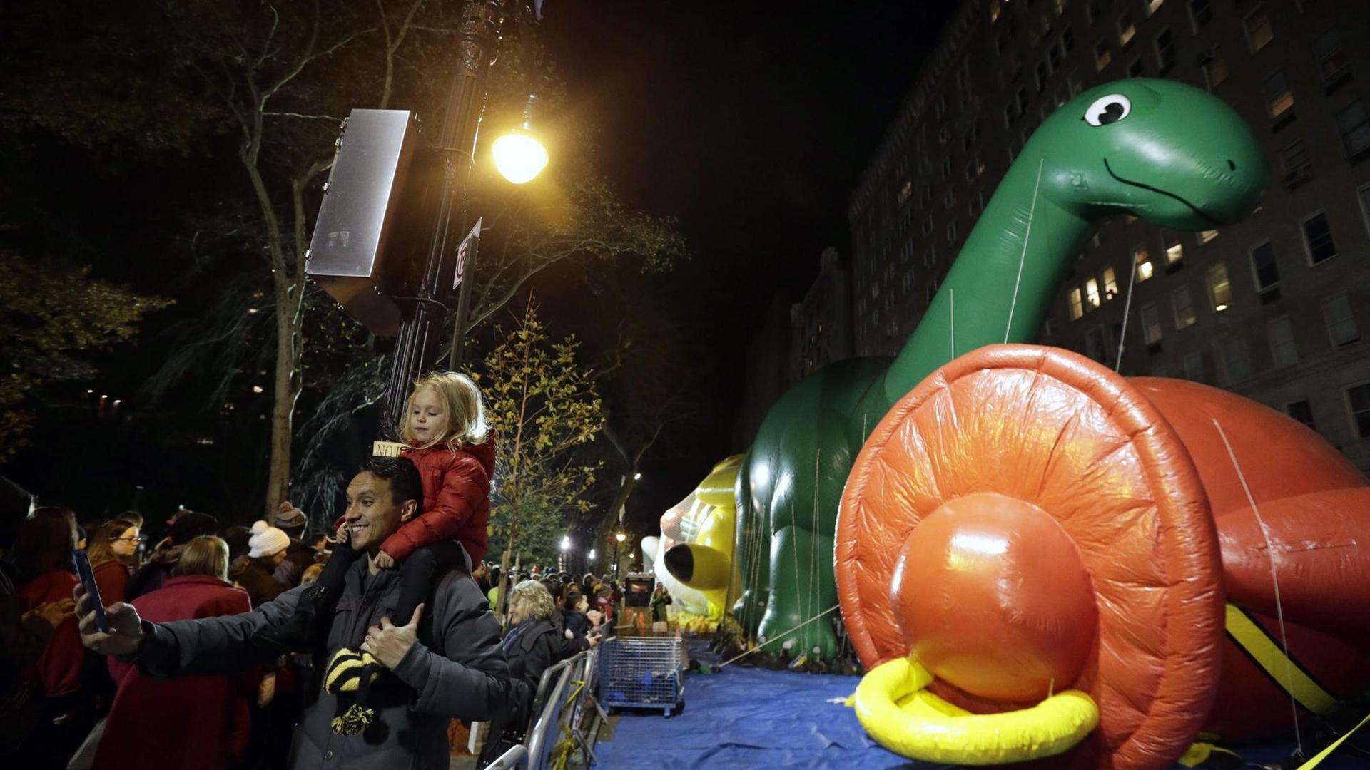 Ein Vater und ein Kind vor einem aufgeblasenem Dinosaurier der Macy's Thanksgiving Day Parade 2015 in New York.