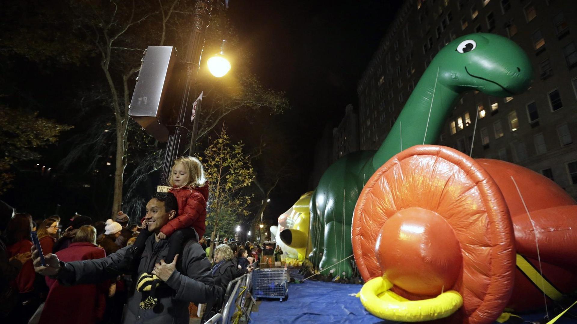 Ein Vater und ein Kind vor einem aufgeblasenem Dinosaurier der Macy's Thanksgiving Day Parade 2015 in New York. Ein Vater und ein Kind vor einem aufgeblasenem Dinosaurier der Macy's Thanksgiving Day Parade 2015 in New York.