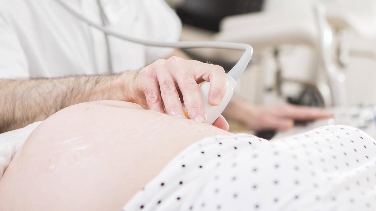 Die Hand eines Arztes mit einem Ultraschallgerät auf dem Bauch einer Schwangeren.