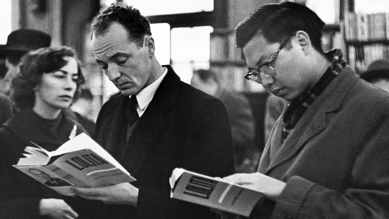 Schwarzweiss Fotografie zweier Männer in einer Londoner Buchhandlung. In den Händen halten beide ein aufgeschlagenes Exemplar des Romans "Lolita", 1959.