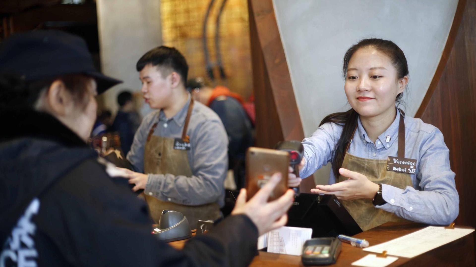 Eine chinesische Mitarbeiterin scannt den QR-Code über den mobilen Bezahldienst Alipay der Alibaba Group auf dem Smartphone eines Kunden. Foto: Bai Kelin/HPIC/dpa Eine chinesische Mitarbeiterin scannt den QR-Code über den mobilen Bezahldienst Alipay der Alibaba Group auf dem Smartphone eines Kunden. Foto: Bai Kelin/HPIC/dpa