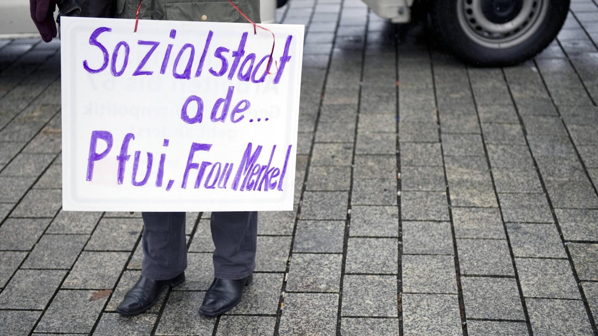 Eine Demonstrantin mit einem Schild auf dem Steht: "Sozialstaat ade Pfui Frau Merkel" Symbolfoto,
