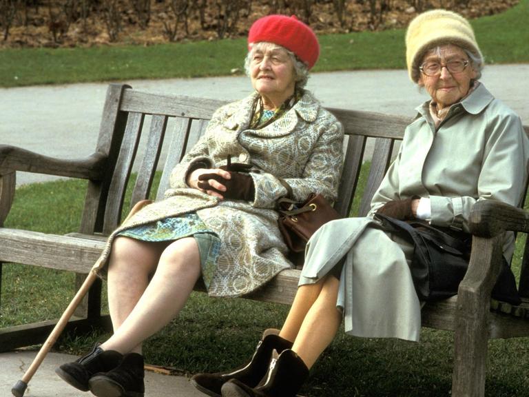 Zwei ältere Damen sitzen auf einer Parkbank.