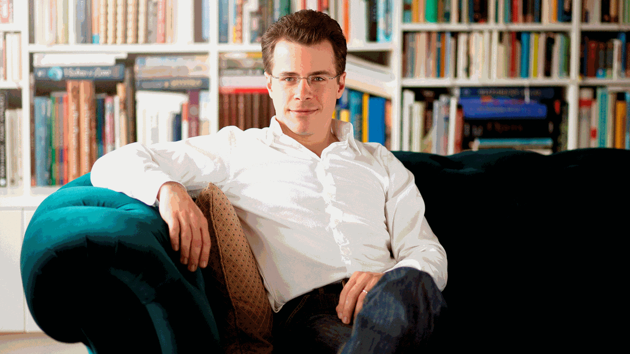 Der Dirigent Jakub Hrůša sitzt auf einem grünen Sofa umgeben von Regalen voller Noten und Bücher. Der Dirigent Jakub Hrůša sitzt auf einem grünen Sofa umgeben von Regalen voller Noten und Bücher.