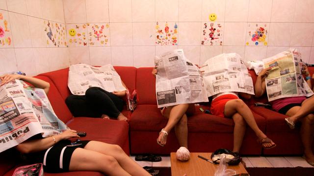 Indonesische Prostituierte sitzen in einem Hotel und verstecken ihre Köpfe hinter Zeitungen.