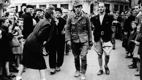 Französische Soldaten führen einen deutschen Kriegsgefangenen, der von der Bevölkerung beschimpft wird, ab - Sommer 1944.