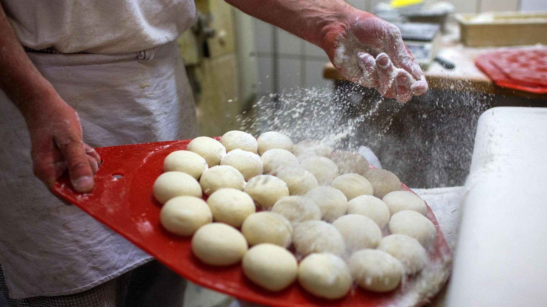 Bäcker bestäubt Teigrundlinge mit Mehl Bäcker bestäubt Teigrundlinge mit Mehl