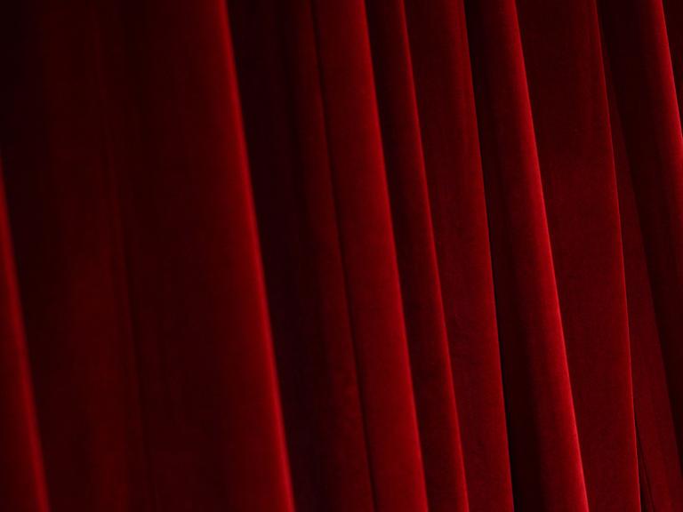 Blick auf einen schweren, roten, Falten werfenden Bühnenvorhang