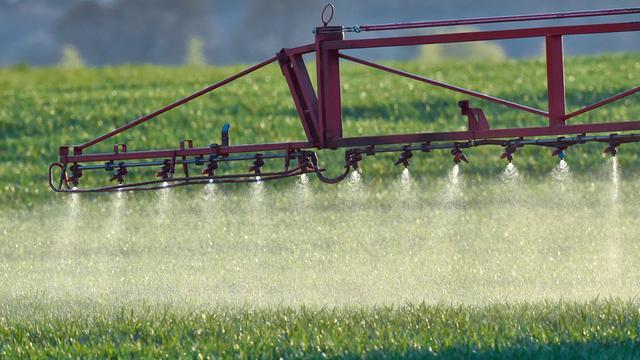 Ein Landwirt fährt mit einer Dünger- und Pestizidspritze über ein Feld.  
