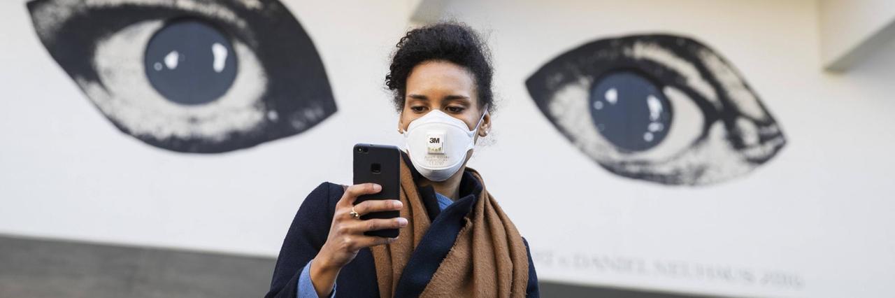Eine Junge Frau schaut auf ihr Handy mit den Augen eines Grafitti im Hintergrund. Eine Junge Frau schaut auf ihr Handy mit den Augen eines Grafitti im Hintergrund.