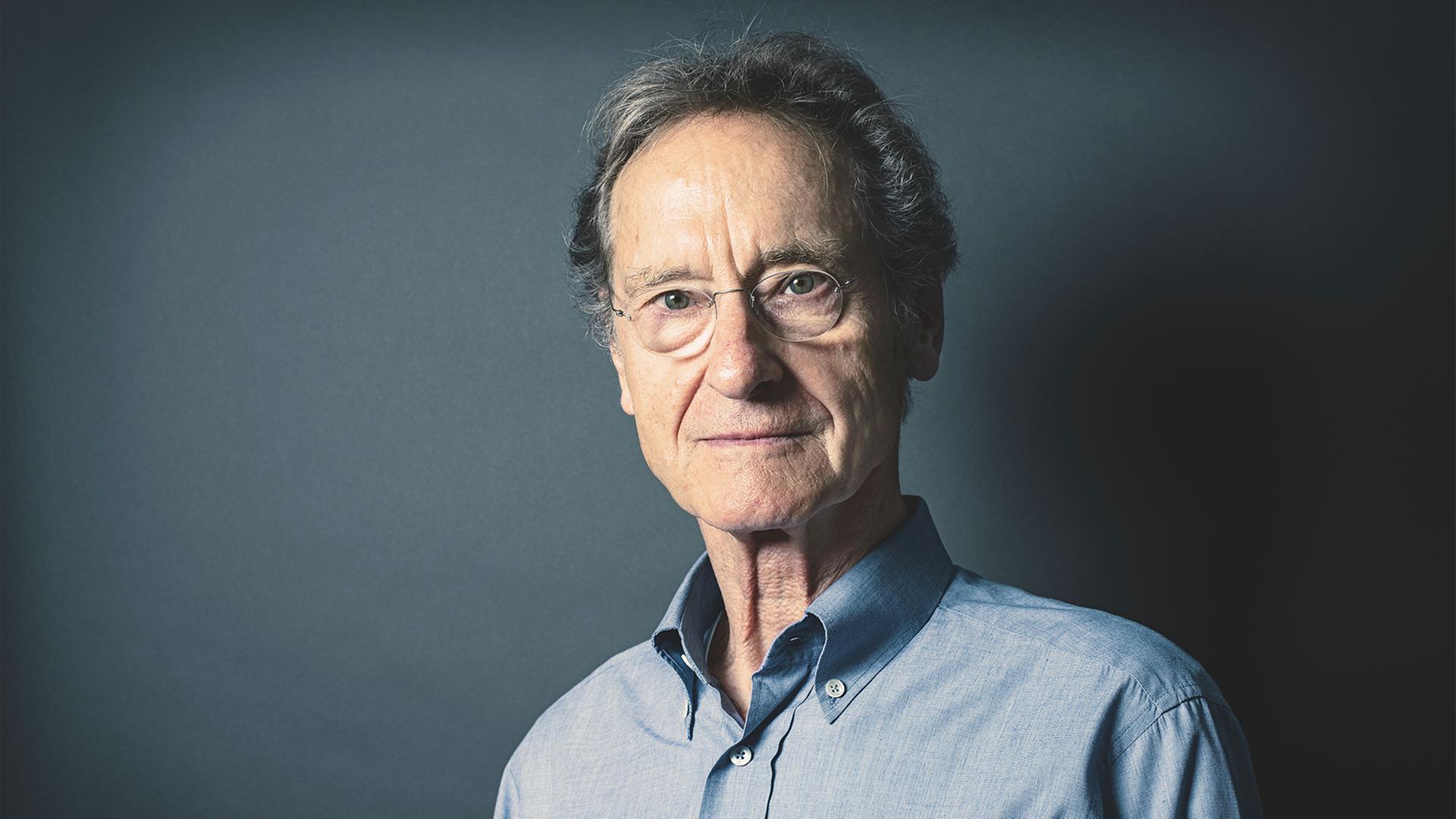 Bernhard Schlink steht vor einem blaugrauem Hintergrund und schaut in die Kamera. Bernhard Schlink steht vor einem blaugrauem Hintergrund und schaut in die Kamera.