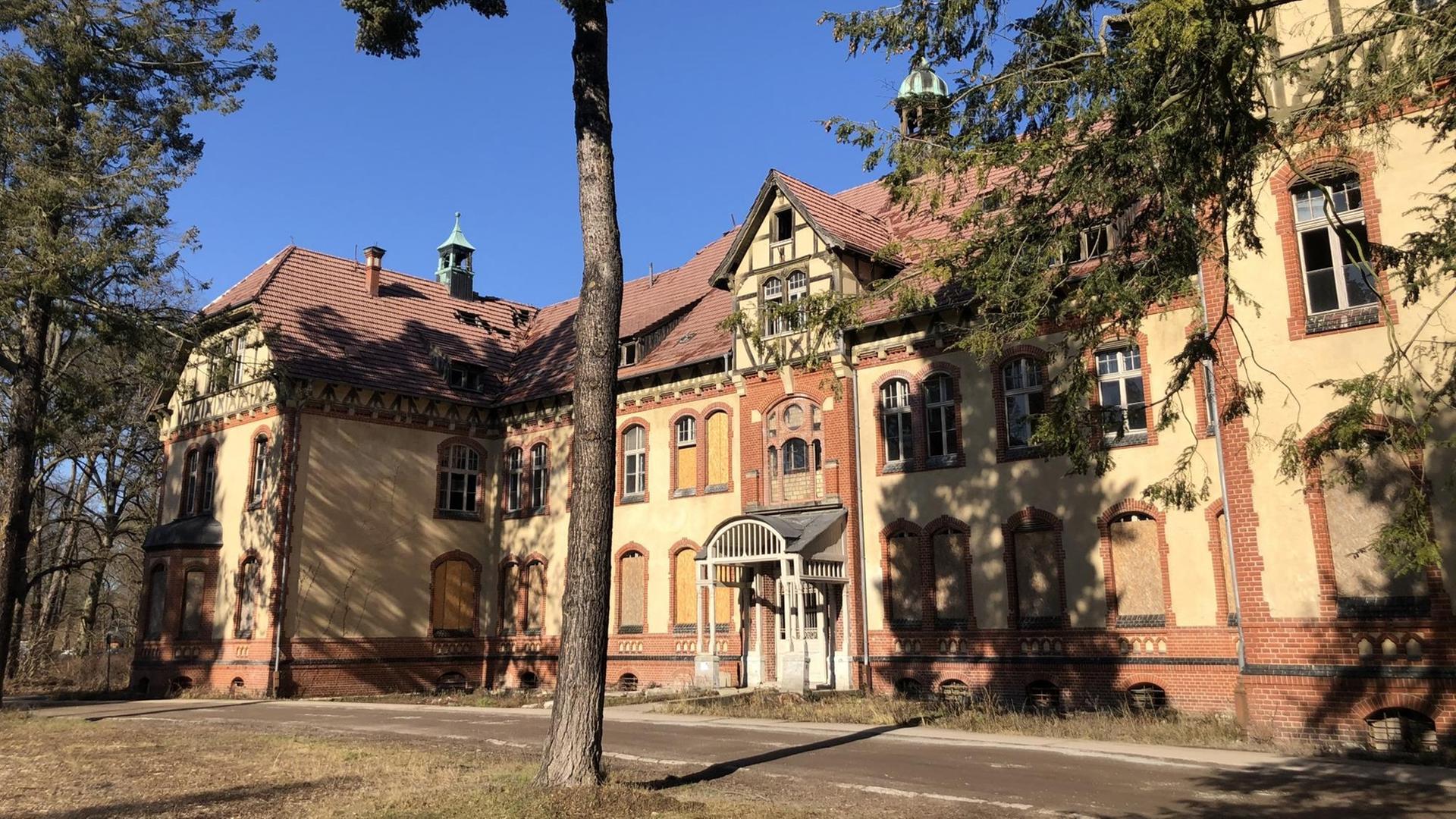 Ein prachtvoller Bau mit Rasen und hoch gewachsenen Bäumem im Vordergrund erstrahlt im Sonnenlicht. Die Fassade enthält Klinkerflächen und gelb angemalte Flächen. Ein prachtvoller Bau mit Rasen und hoch gewachsenen Bäumem im Vordergrund erstrahlt im Sonnenlicht. Die Fassade enthält Klinkerflächen und gelb angemalte Flächen.