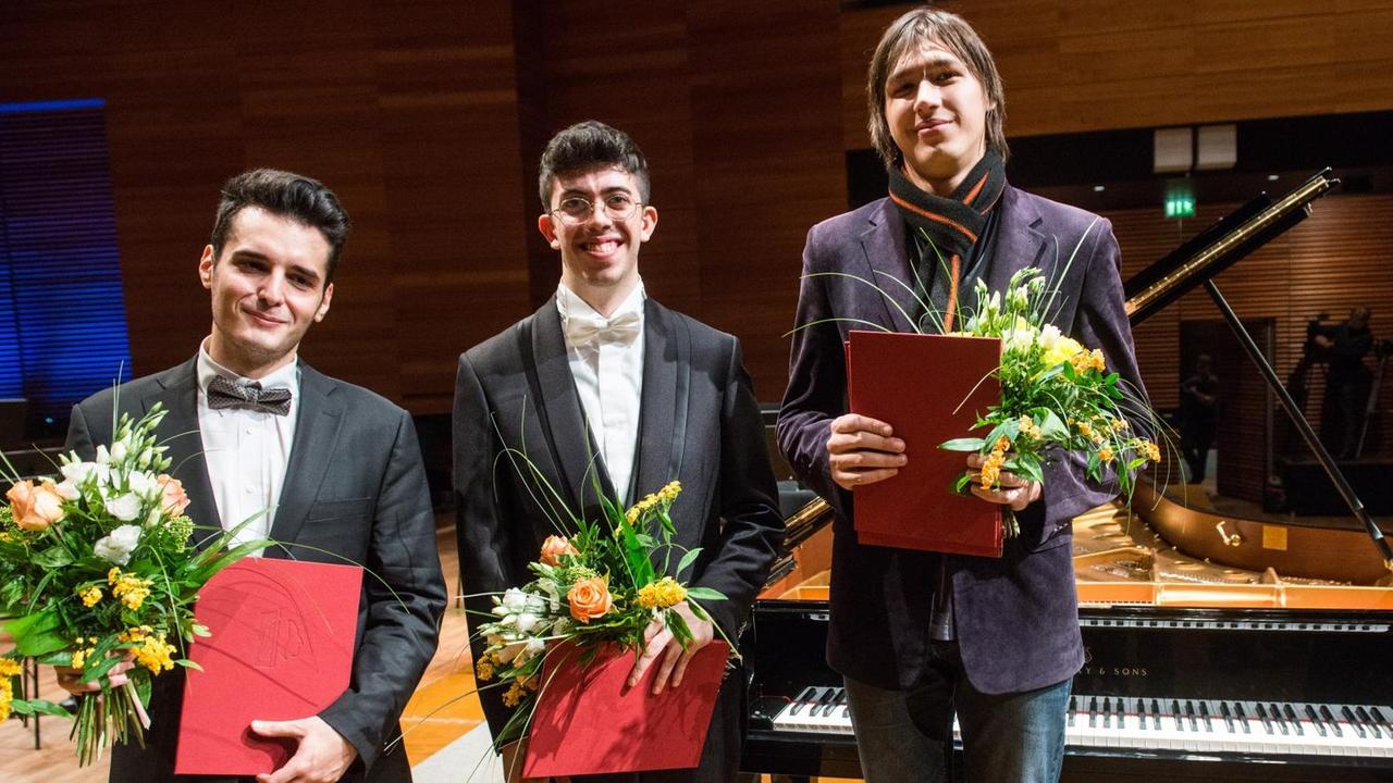 Die Gewinner stehen mit Blumensträußen und Urkunden vor einem Flügel Die Gewinner stehen mit Blumensträußen und Urkunden vor einem Flügel