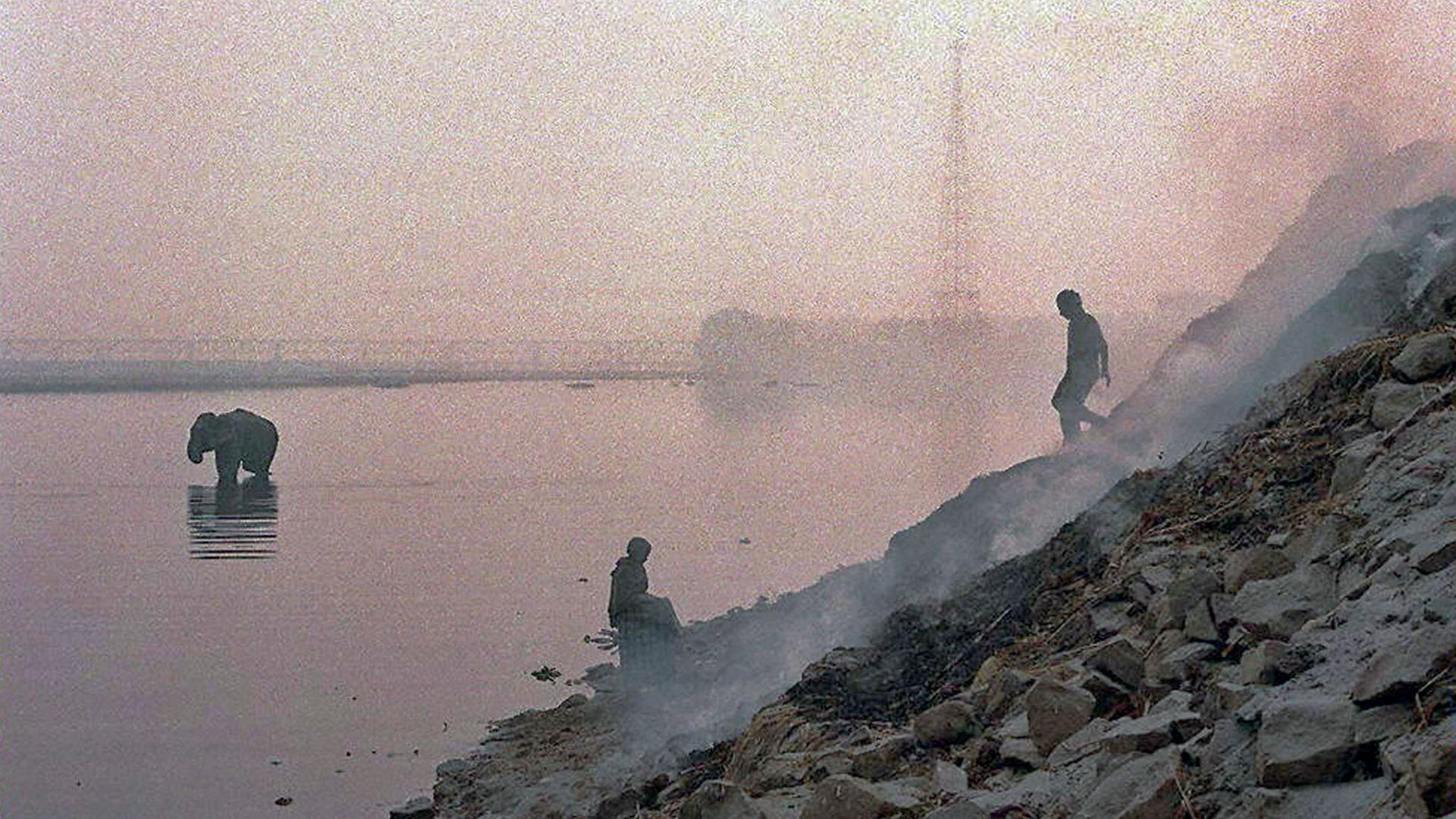 Zwei Männern und ein Elefant sind in der dunstigen Luft neben einem brennender Müllhalde am Yamuna Fluß in Neu Delhi nur als Umriss zu erkennen. Der heilige Yamuna Fluß ist stark durch industrielle Abwässer verschmutzt. Zwei Männern und ein Elefant sind in der dunstigen Luft neben einem brennender Müllhalde am Yamuna Fluß in Neu Delhi nur als Umriss zu erkennen. Der heilige Yamuna Fluß ist stark durch industrielle Abwässer verschmutzt.