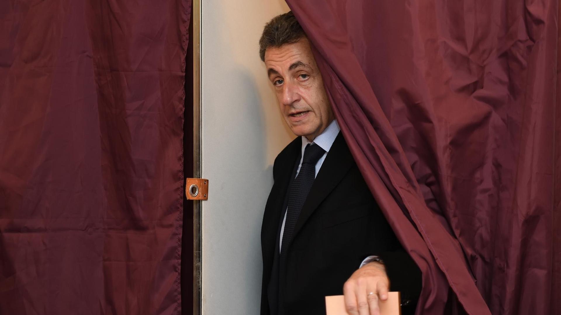 Frankreichs früherer Präsident Nicolas Sarkozy kommt mit einem Wahlzettel in der Hand aus der Kabine Frankreichs früherer Präsident Nicolas Sarkozy kommt mit einem Wahlzettel in der Hand aus der Kabine