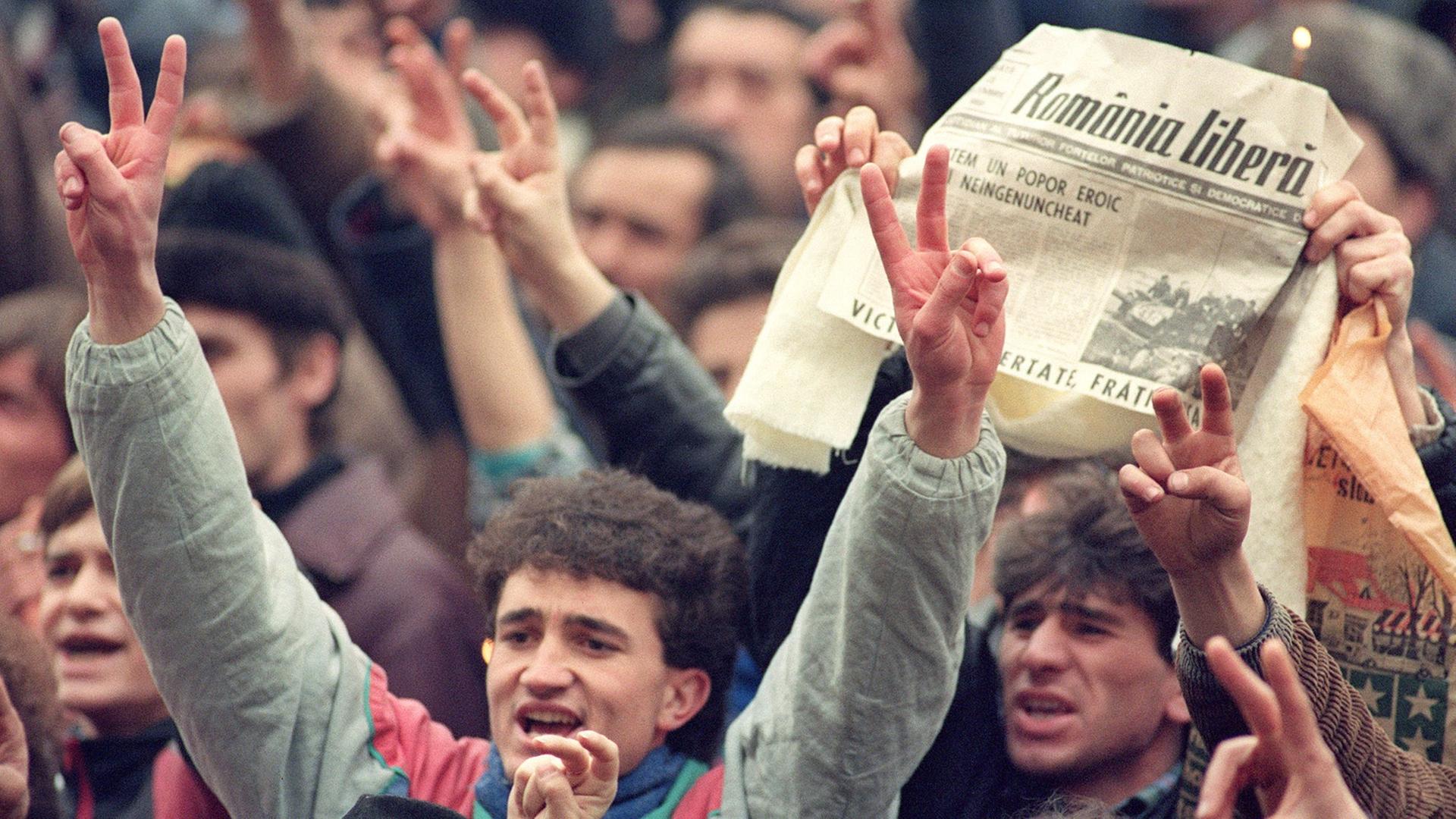 Tausende Rumänen jubeln am 24. Dezember 1989 in den Straßen von Bukarest. In der Zeitung ist zu lesen, dass Diktator Ceausescu und seine Frau verhaftet wurden.