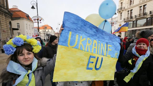 Menschen demonstrieren mit gelb-blauen Plakaten für einen EU-Beitritt der Ukraine