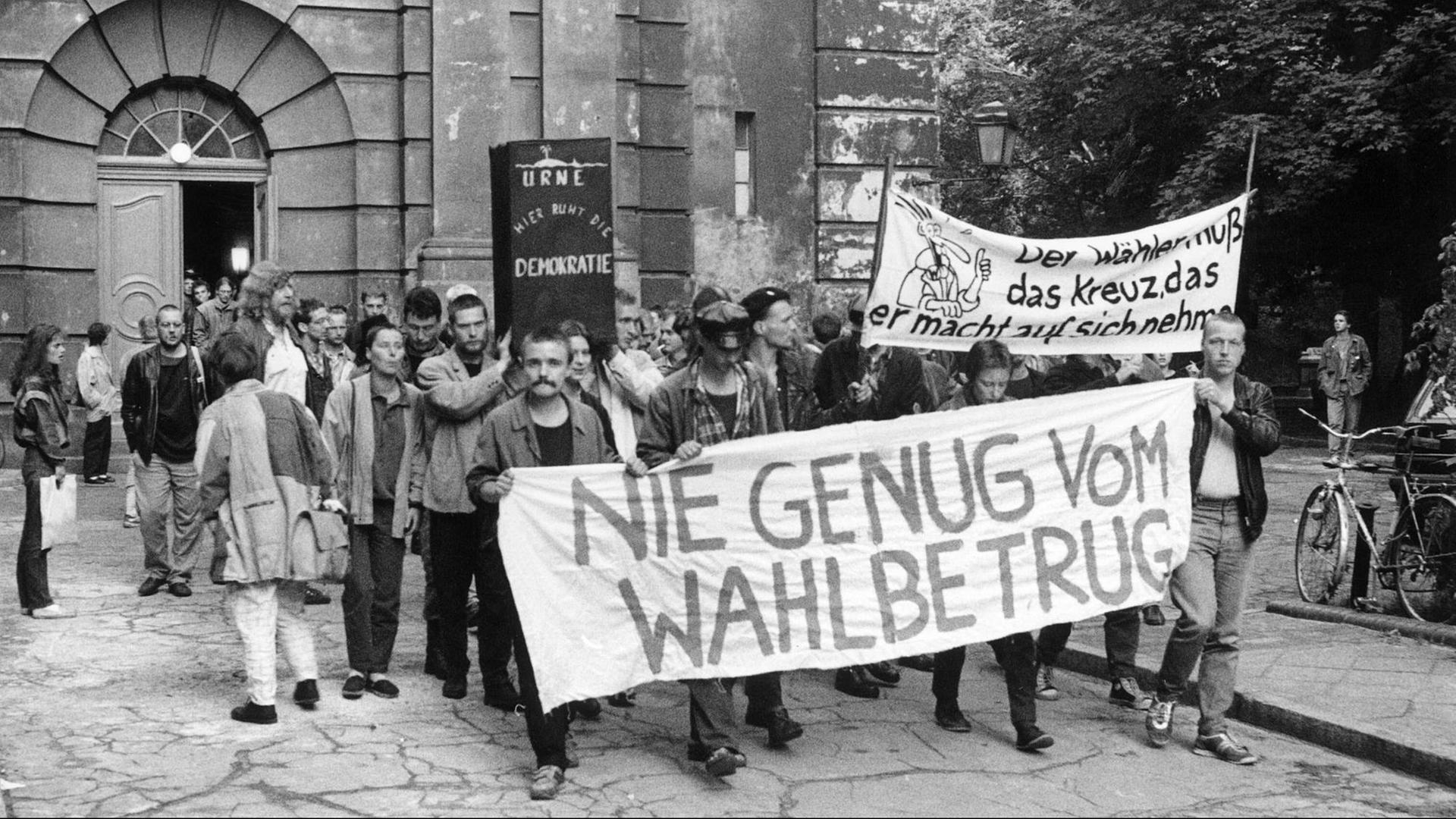 Eine Gruppe von Menschen steht vor einer Kirche und trägt Banner, im Vordergrund eines mit der Aufschrift "Nie genug vom Wahlbetrug". Eine Gruppe von Menschen steht vor einer Kirche und trägt Banner, im Vordergrund eines mit der Aufschrift "Nie genug vom Wahlbetrug".