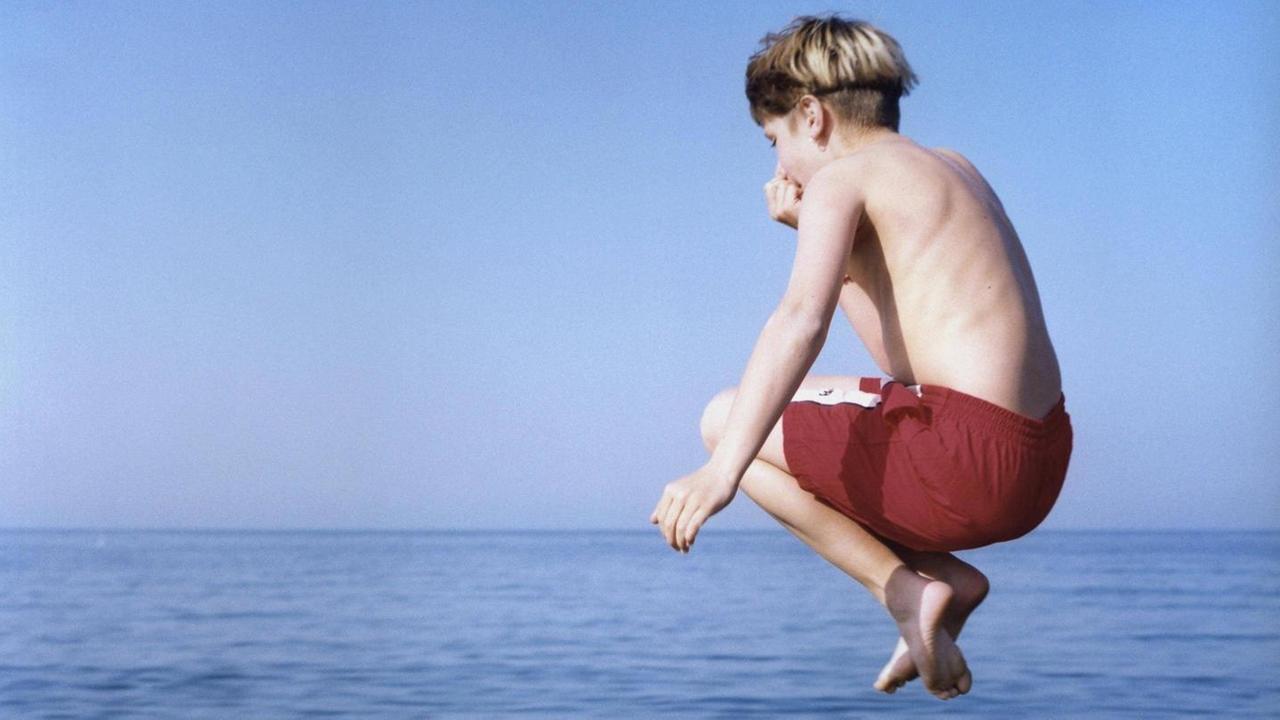 Eine Junge springt ins Meer.