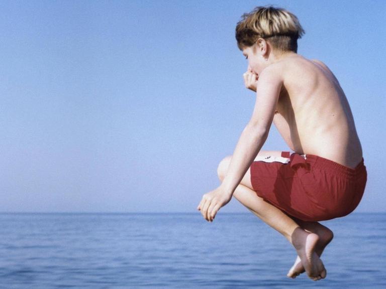 Eine Junge springt ins Meer.
