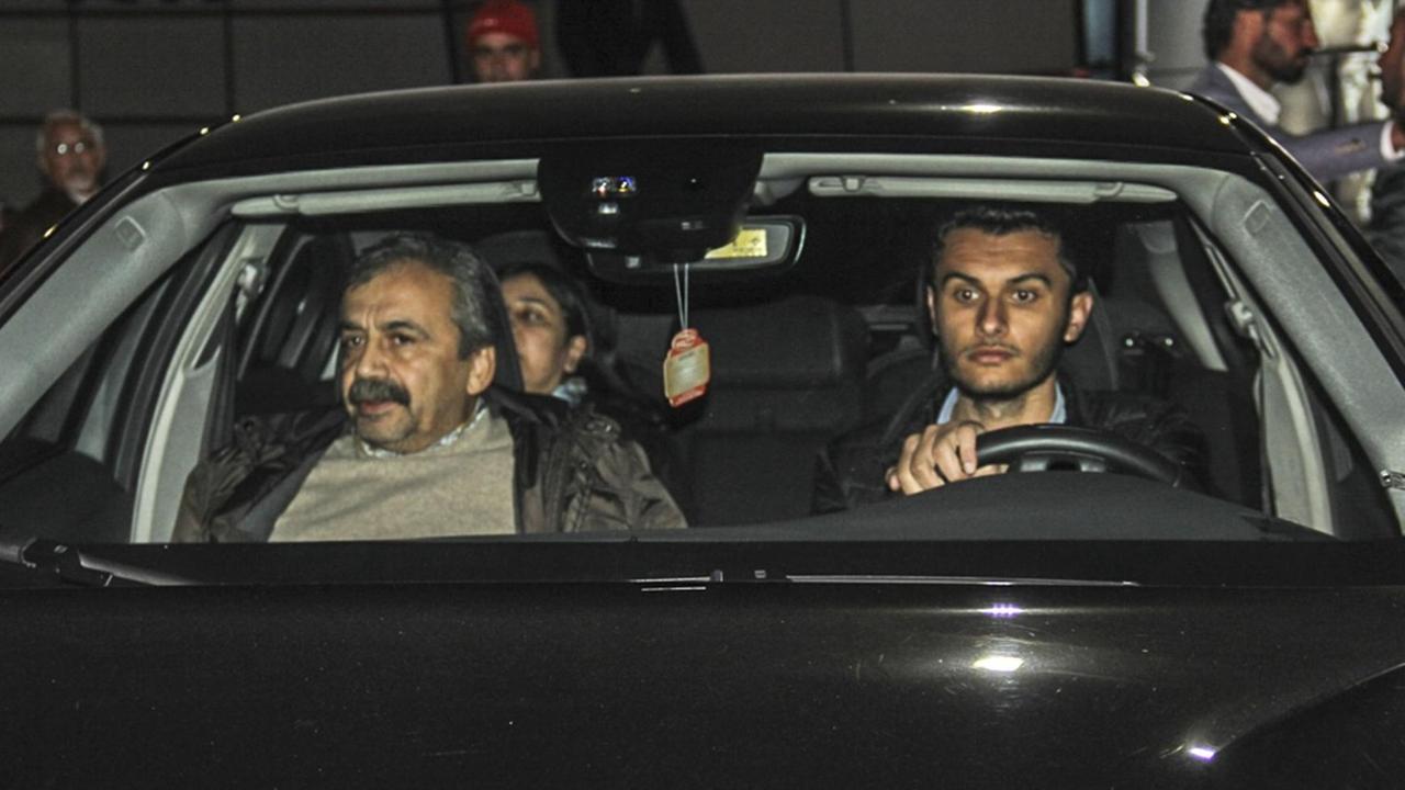 Sirri Süreyya Önder auf dem Beifahrersitz eines schwarzen Autos, ein anderer Mann fährt das Fahrzeug. Sirri Süreyya Önder auf dem Beifahrersitz eines schwarzen Autos, ein anderer Mann fährt das Fahrzeug.