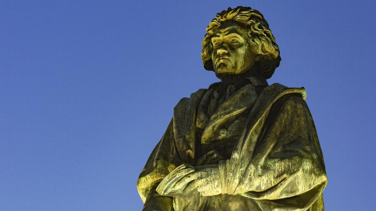 Denkmal am Münsterplatz in Bonn: der Komponist und Pianist Ludwig van Beethoven angestrahlt vor abendlichem Himmel.