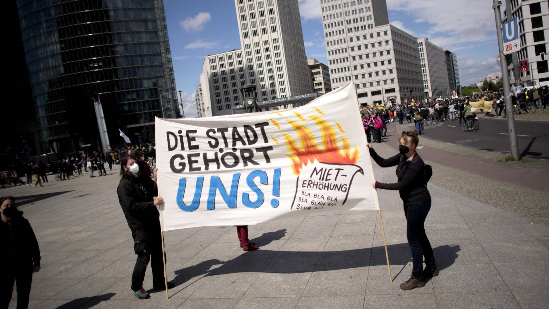 Zwischen Hochhäusern laufen Demonstranten mit einem Plakat "Die Stadt gehört uns". Zwischen Hochhäusern laufen Demonstranten mit einem Plakat "Die Stadt gehört uns".