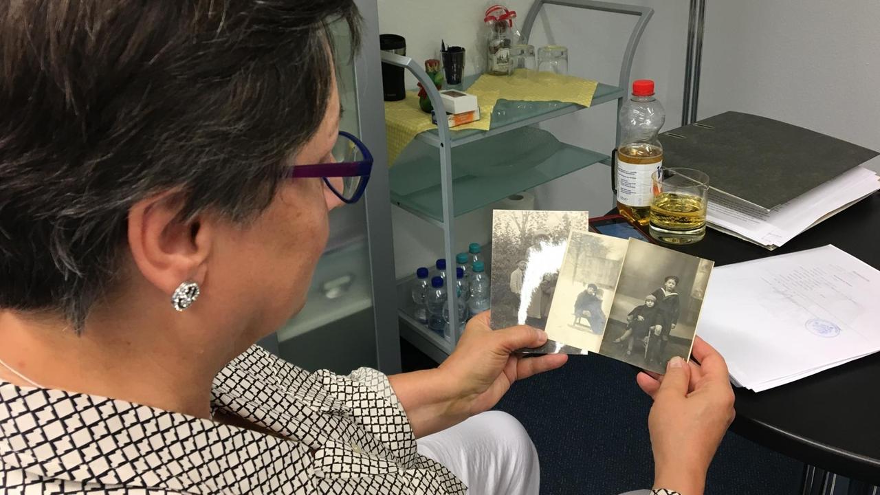 Gisela Puschmann sitzt an einem Tisch und hält drei vergilbte Schwarz-weiß-Fotos in der Hand