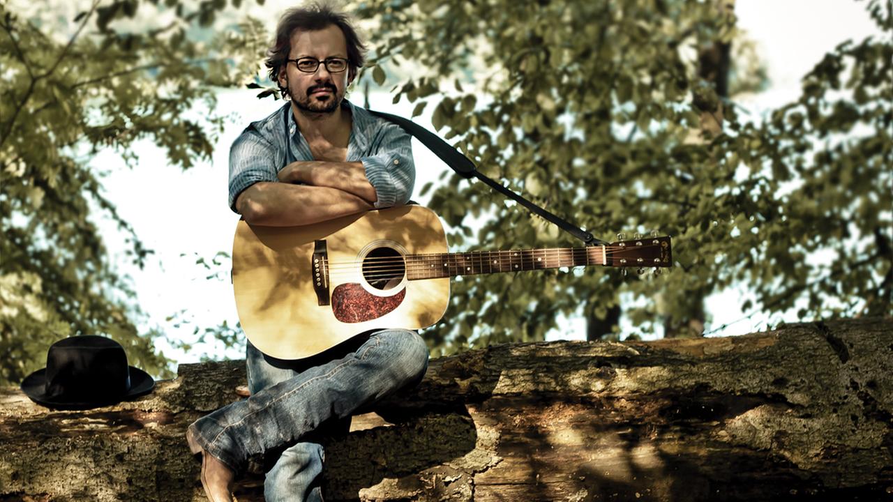 Tobias Panwitz aka. Trailhead sitzt auf einem Baumstamm mit einer Gitarre auf dem Schoß Tobias Panwitz aka. Trailhead sitzt auf einem Baumstamm mit einer Gitarre auf dem Schoß