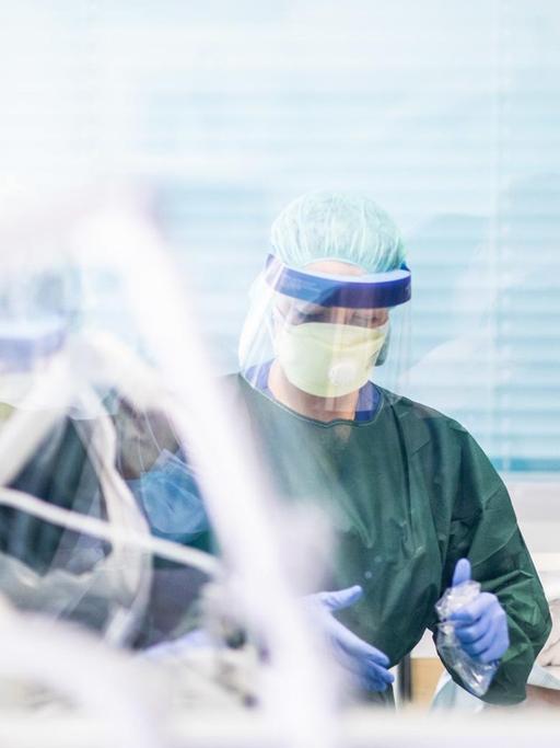 Zwei Krankenpfleger arbeiten in Schutzkleidung in einem Krankenzimmer auf der Intensivstation des Uniklinikums Essen, in dem ein Corona-Patient aus Frankreich behandelt wird.