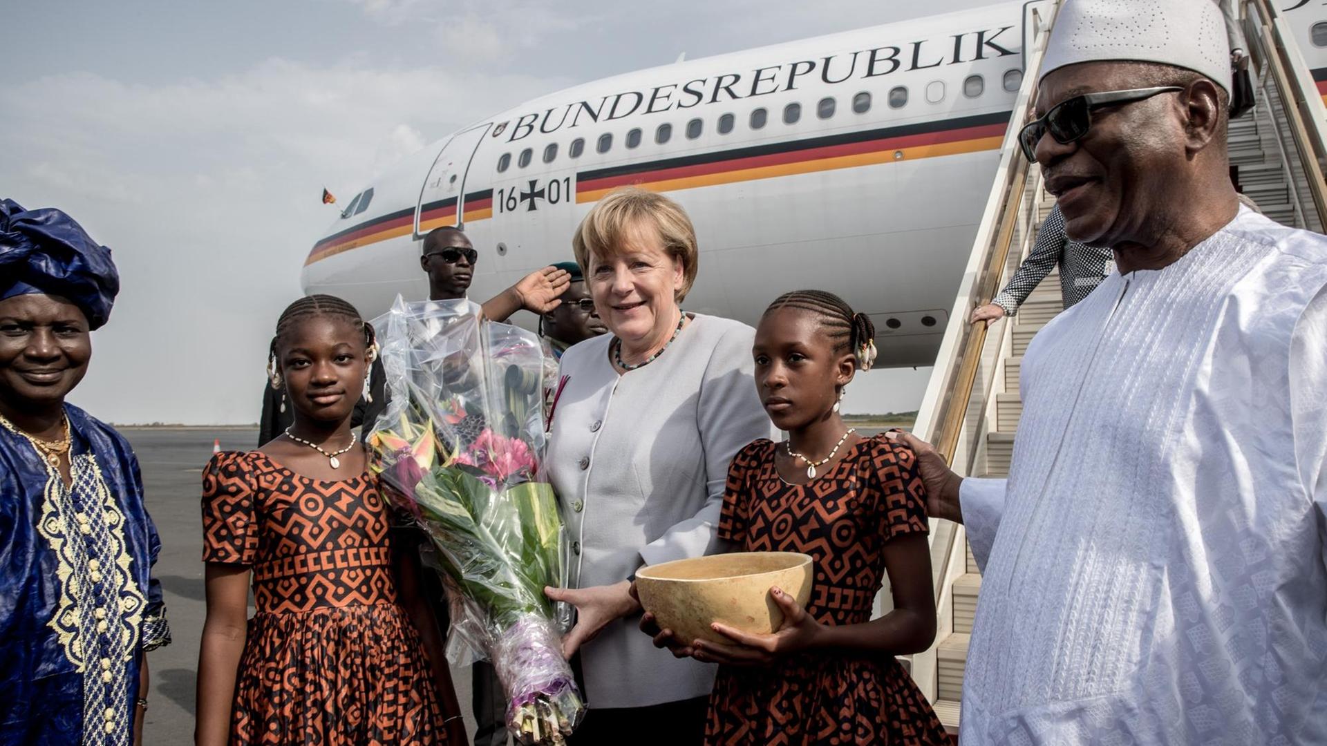Bundeskanzlerin Angela Merkel steht in Mali vor der Regierungsmaschine. Neben ihr stehen zwei Mädchen mit Blumen und einer traditionellen Wasserkalebasse. Auch Staatspräsident Ibrahim Boubacar Keita ist auf dem Bild zu sehen. Bundeskanzlerin Angela Merkel steht in Mali vor der Regierungsmaschine. Neben ihr stehen zwei Mädchen mit Blumen und einer traditionellen Wasserkalebasse. Auch Staatspräsident Ibrahim Boubacar Keita ist auf dem Bild zu sehen.