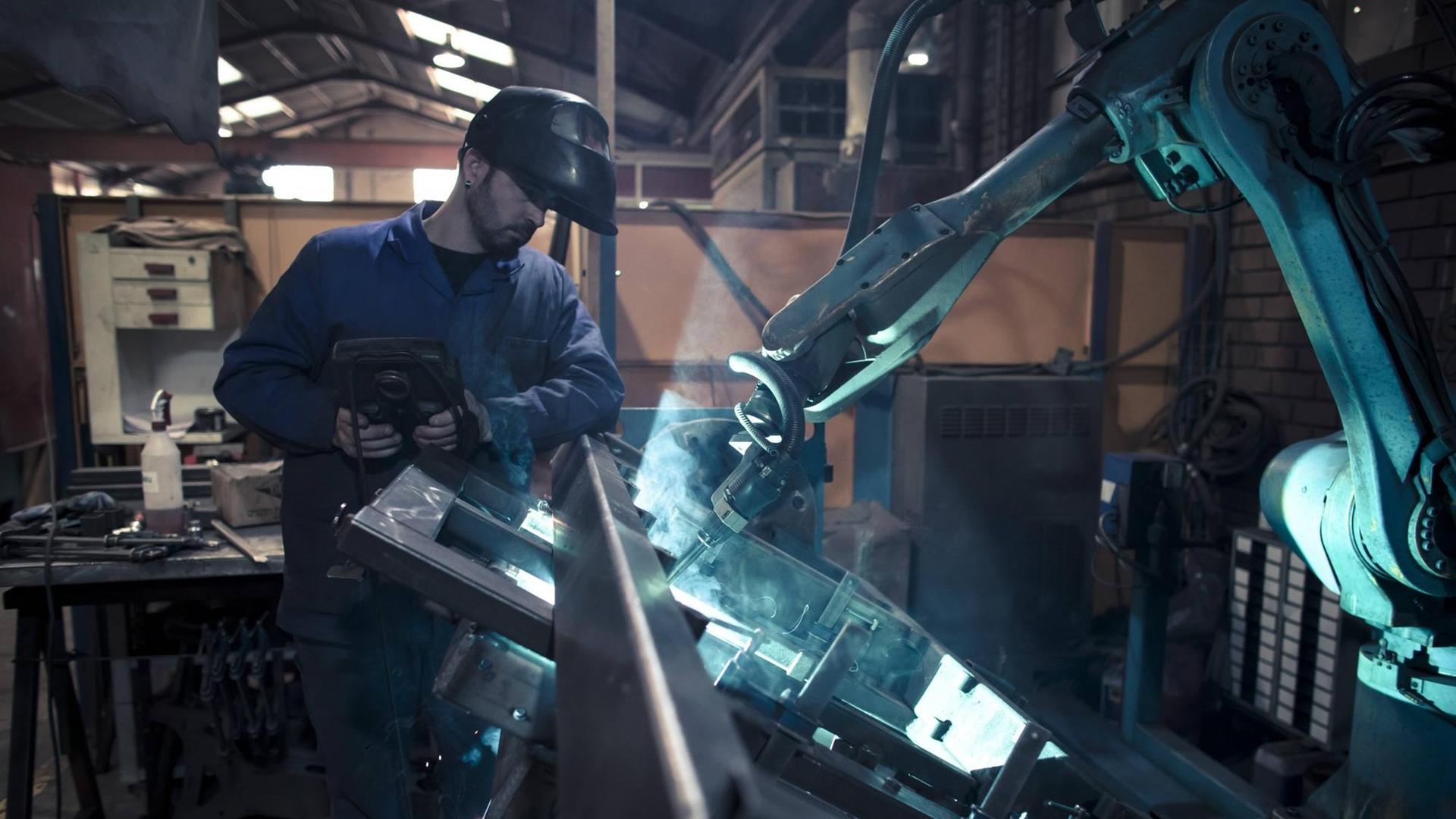 Ein Mann schweißt gemeinsam mit einem Roboter Metall (Symbol-Foto). Ein Mann schweißt gemeinsam mit einem Roboter Metall (Symbol-Foto).