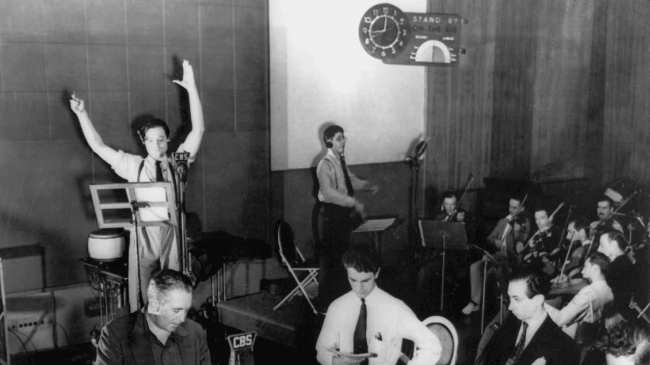 Schwarz-weiß-Aufnahme einer Hörspiel-Übertragung in einem Studio. Sprecher an Mikrofonen und Musiker mit Geigen. Schwarz-weiß-Aufnahme einer Hörspiel-Übertragung in einem Studio. Sprecher an Mikrofonen und Musiker mit Geigen.