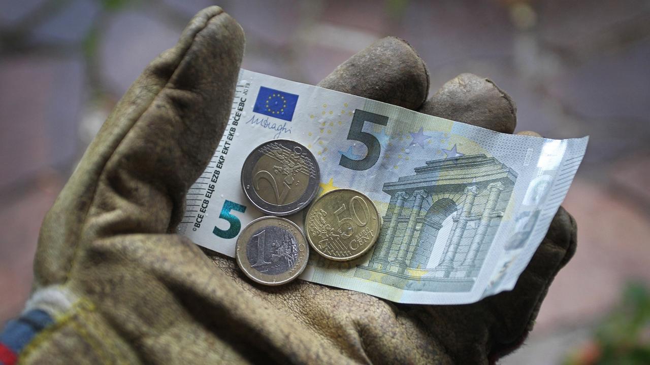 Ein Arbeitshandschuh in dem ein Fünf-Euro-Schein, eine Zwei-Euro-Münze, eine Ein-Euro-Münze sowie ein 50-Cent-Stück liegen. Ein Arbeitshandschuh in dem ein Fünf-Euro-Schein, eine Zwei-Euro-Münze, eine Ein-Euro-Münze sowie ein 50-Cent-Stück liegen.