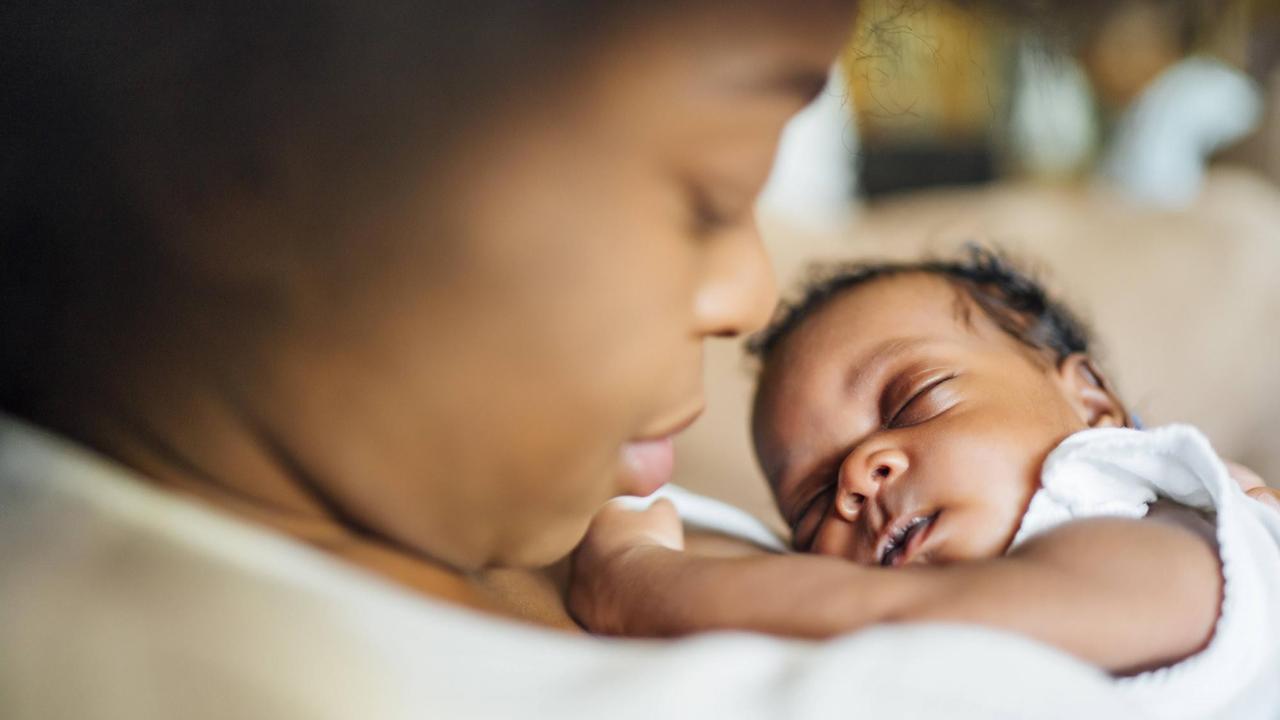 Ein Close-up auf eine Mutter, die ihre schlafende Tochter, ein neugeborenes Baby, auf ihrer Brust liegen hat.