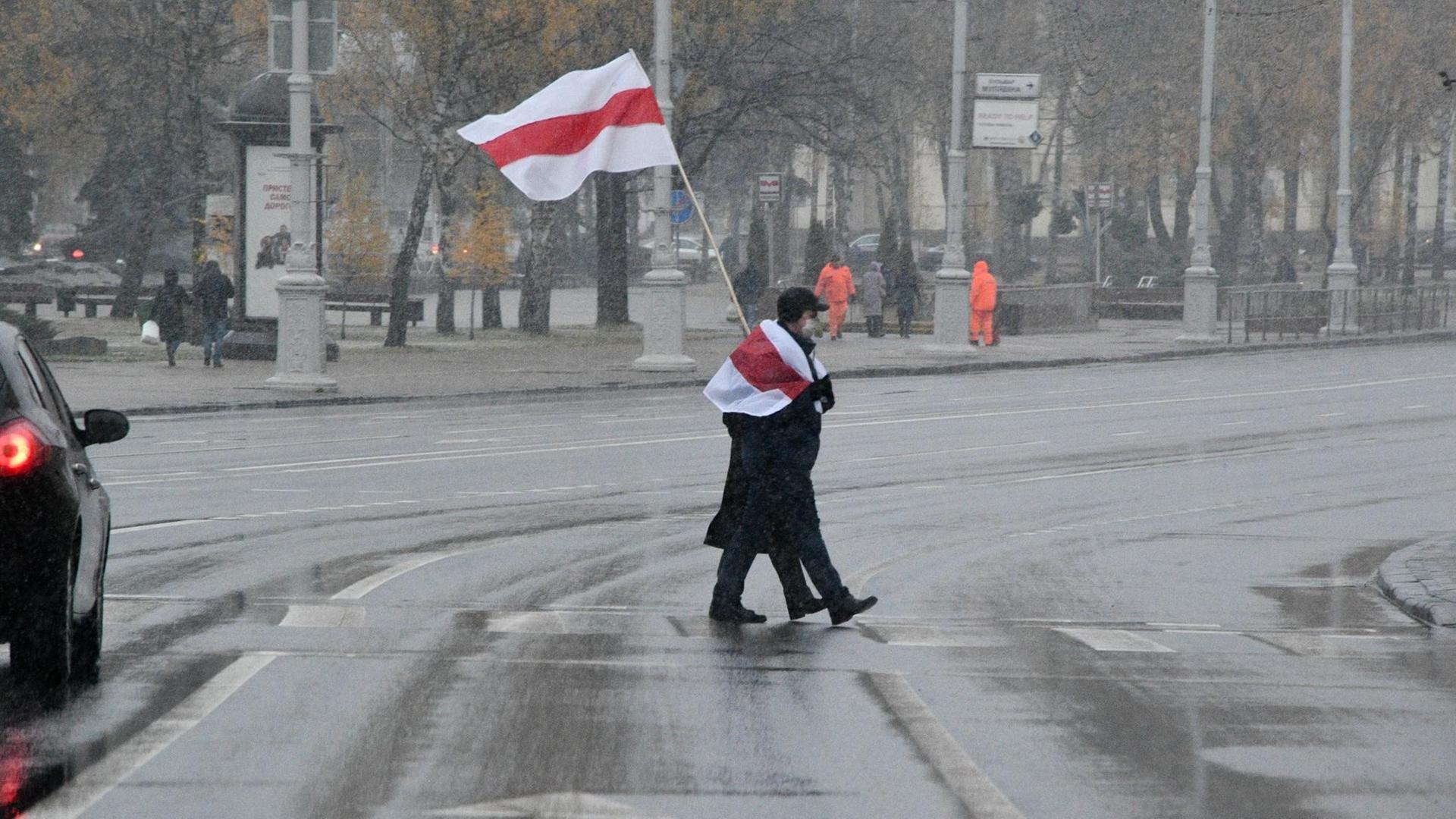 Ein Protestierender mit weiß-rot-weißer Fahne überquert eine Straße in Minsk. Ein Protestierender mit weiß-rot-weißer Fahne überquert eine Straße in Minsk.