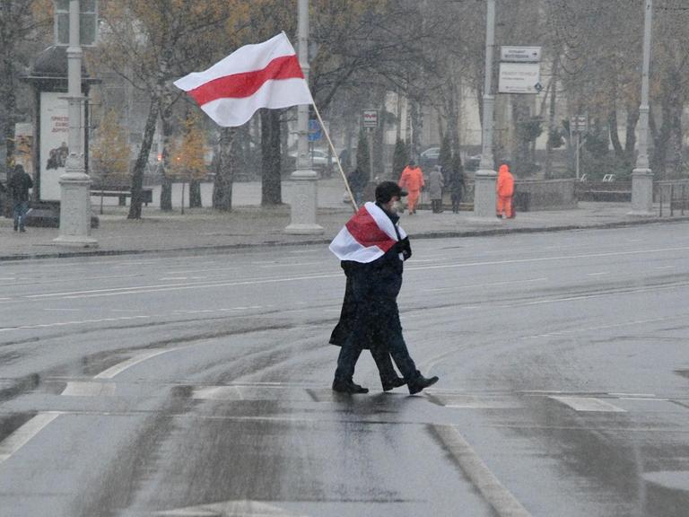 Ein Protestierender mit weiß-rot-weißer Fahne überquert eine Straße in Minsk.