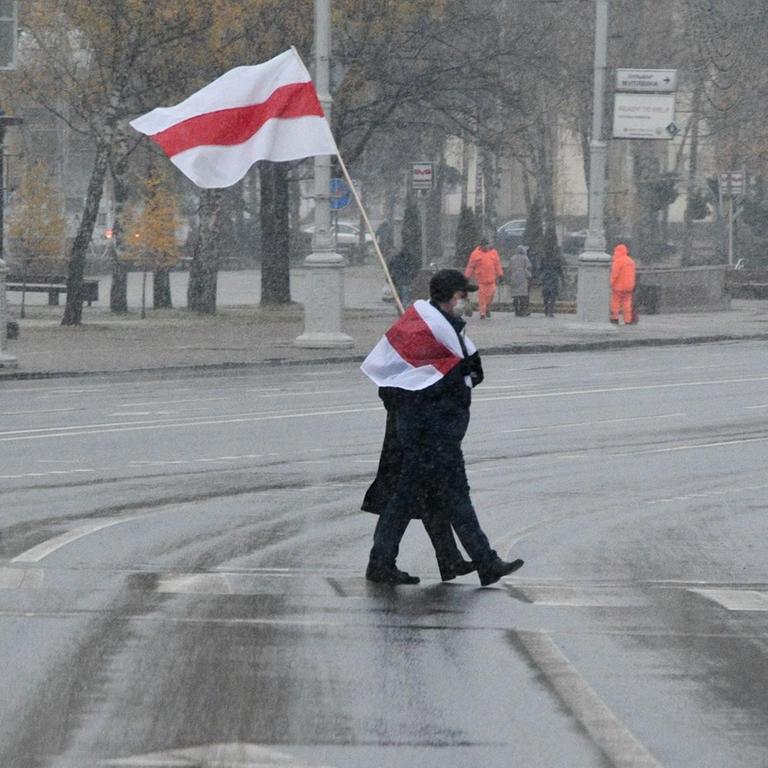 Ein Protestierender mit weiß-rot-weißer Fahne überquert eine Straße in Minsk.