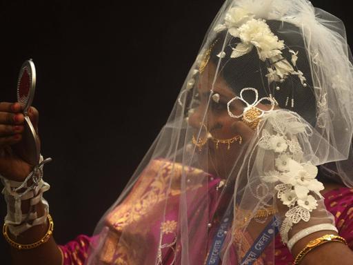 Eine Braut, die in einen kleinen Handspiegel schaut, aufgenommen während einer Massenhochzeit in Kolkata, Indien, am 14. Februar 2021