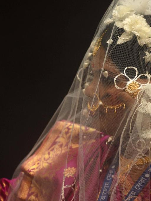 Eine Braut, die in einen kleinen Handspiegel schaut, aufgenommen während einer Massenhochzeit in Kolkata, Indien, am 14. Februar 2021