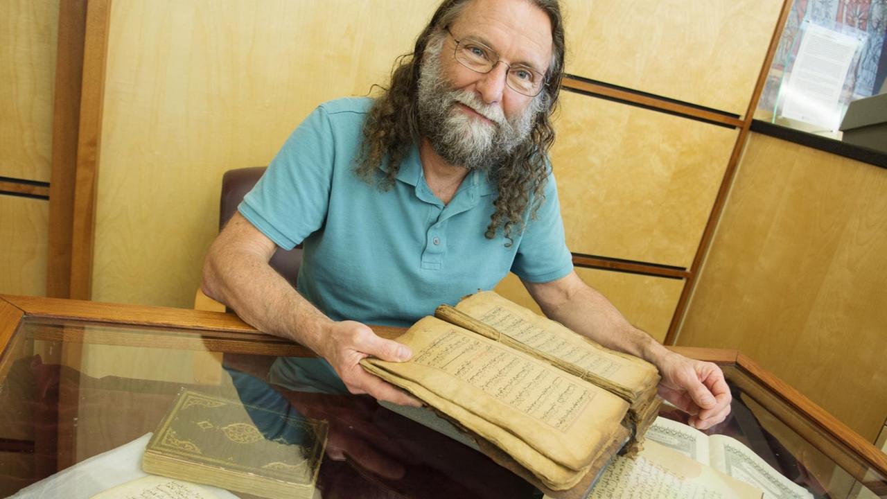 Andrew Rippin vor einem aufgeschlagenen, alten, arabischen Buch. Andrew Rippin vor einem aufgeschlagenen, alten, arabischen Buch.