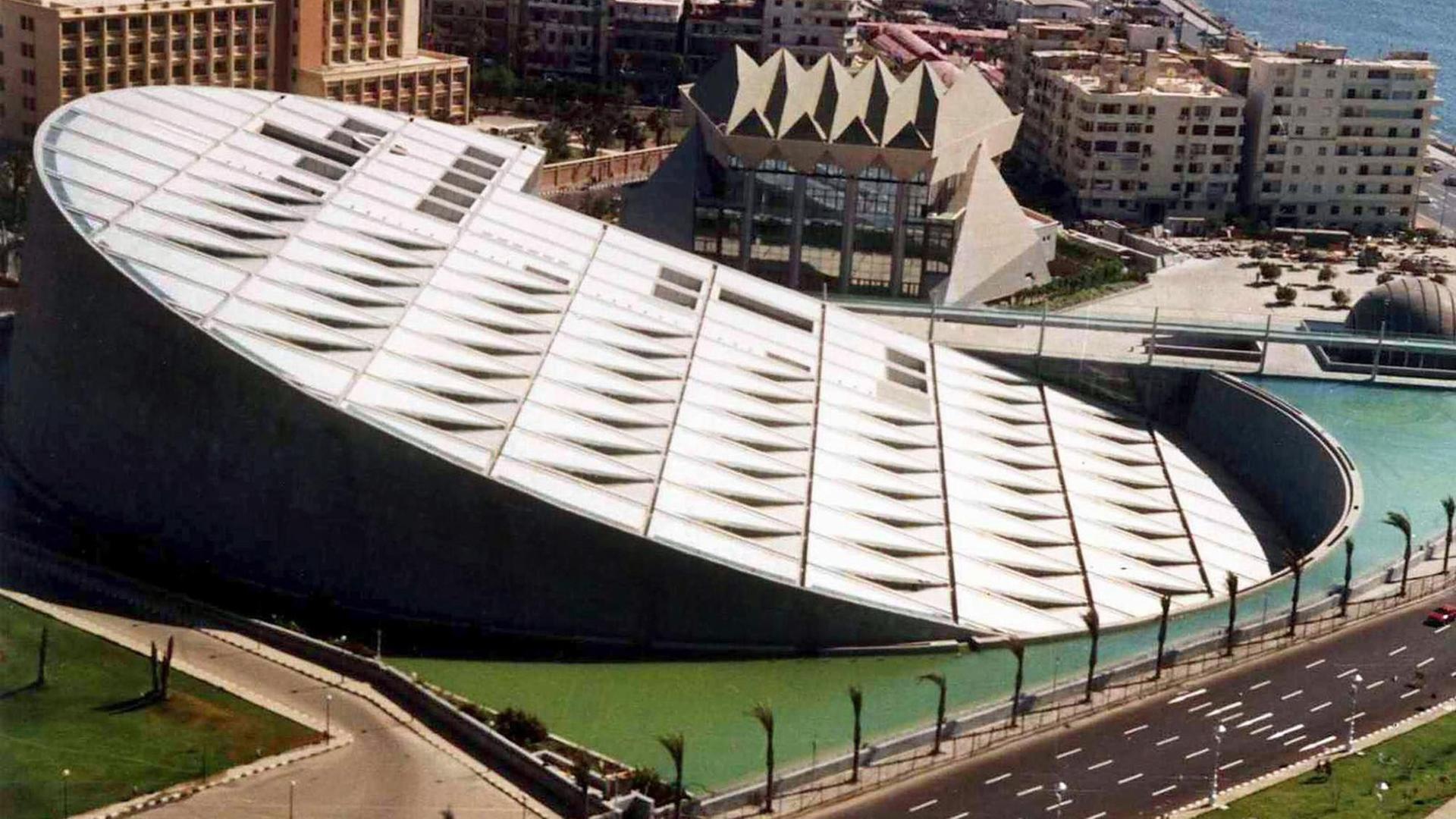 Blick auf die Bibliothek von Alexandria: Ein runder Bau, am Meer gelegen, mit einer schräg abfallenden Seite, in dem Vertiefungen zu erkennen sind. Blick auf die Bibliothek von Alexandria: Ein runder Bau, am Meer gelegen, mit einer schräg abfallenden Seite, in dem Vertiefungen zu erkennen sind.