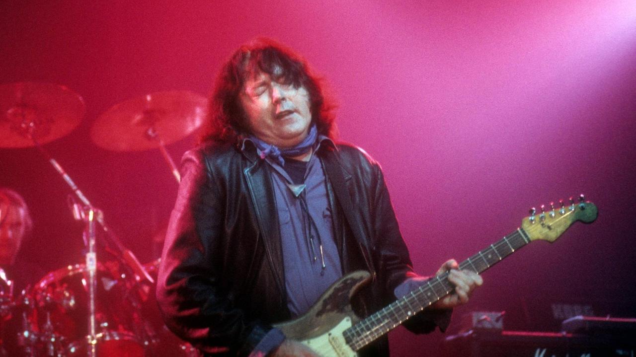 Ein Mann steht auf einer Bühne und spielt Gitarre Ein Mann steht auf einer Bühne und spielt Gitarre