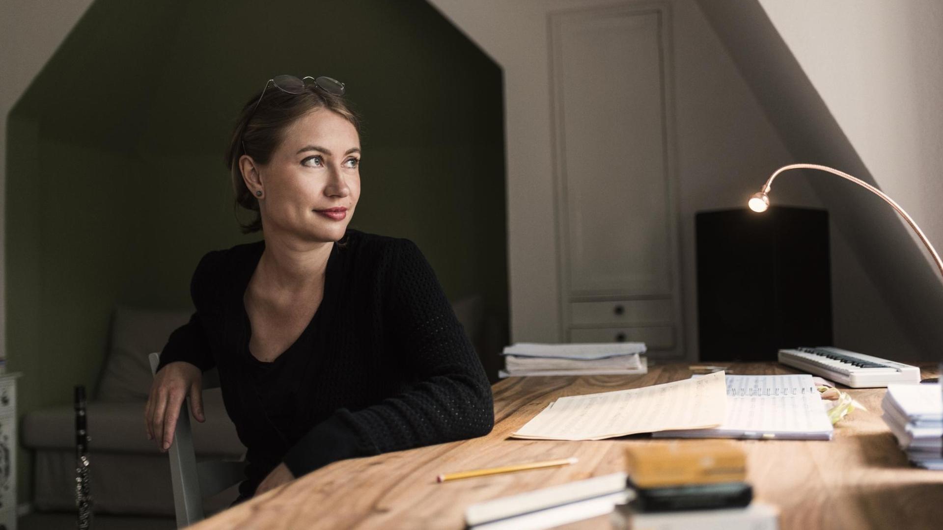 Rebecca Trescher sitzt am Schreibtisch vor einer Komposition Rebecca Trescher sitzt am Schreibtisch vor einer Komposition
