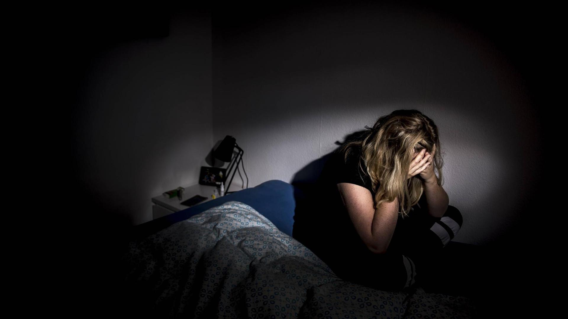 Eine Frau sitzt in ihrem Bett, sie presst ihr Gesicht in ihre Hände Eine Frau sitzt in ihrem Bett, sie presst ihr Gesicht in ihre Hände