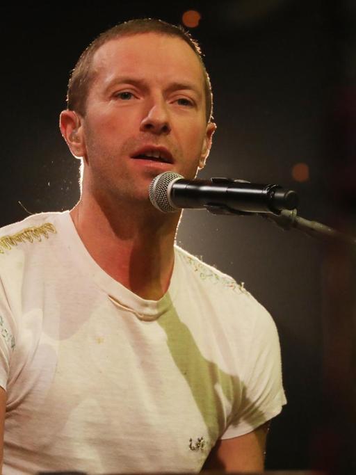 Coldplay-Sänger Christ Martin sitzt bei einem TV-Auftritt in der Graham Norton Show am Flügel. Er trägt ein weißes T-Shirt.